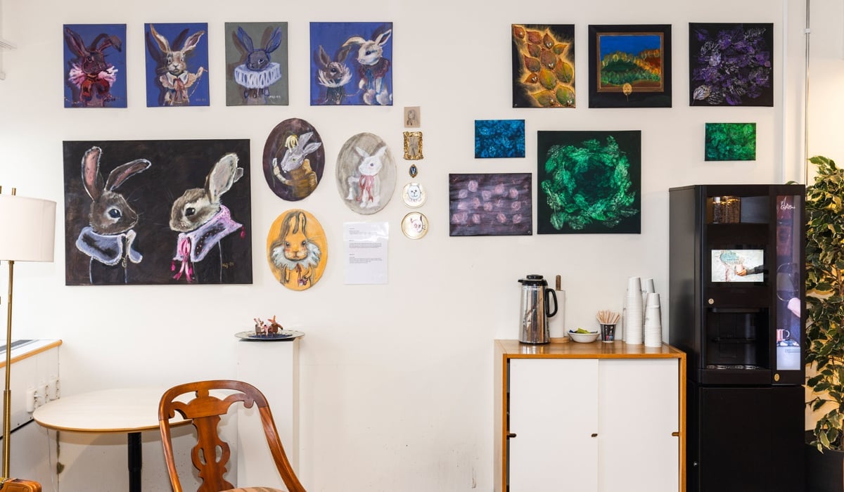 Tavlor utan ram på en vit vägg. Under tavlorna kaffeautomat.