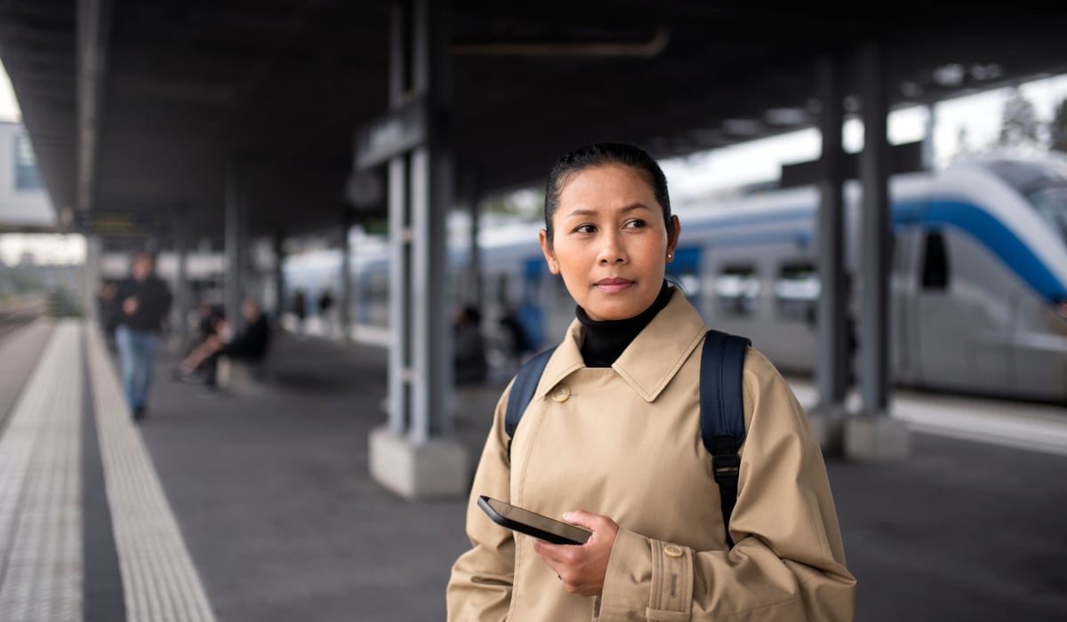 En kvinna står framför ett tåg på en tågstation.