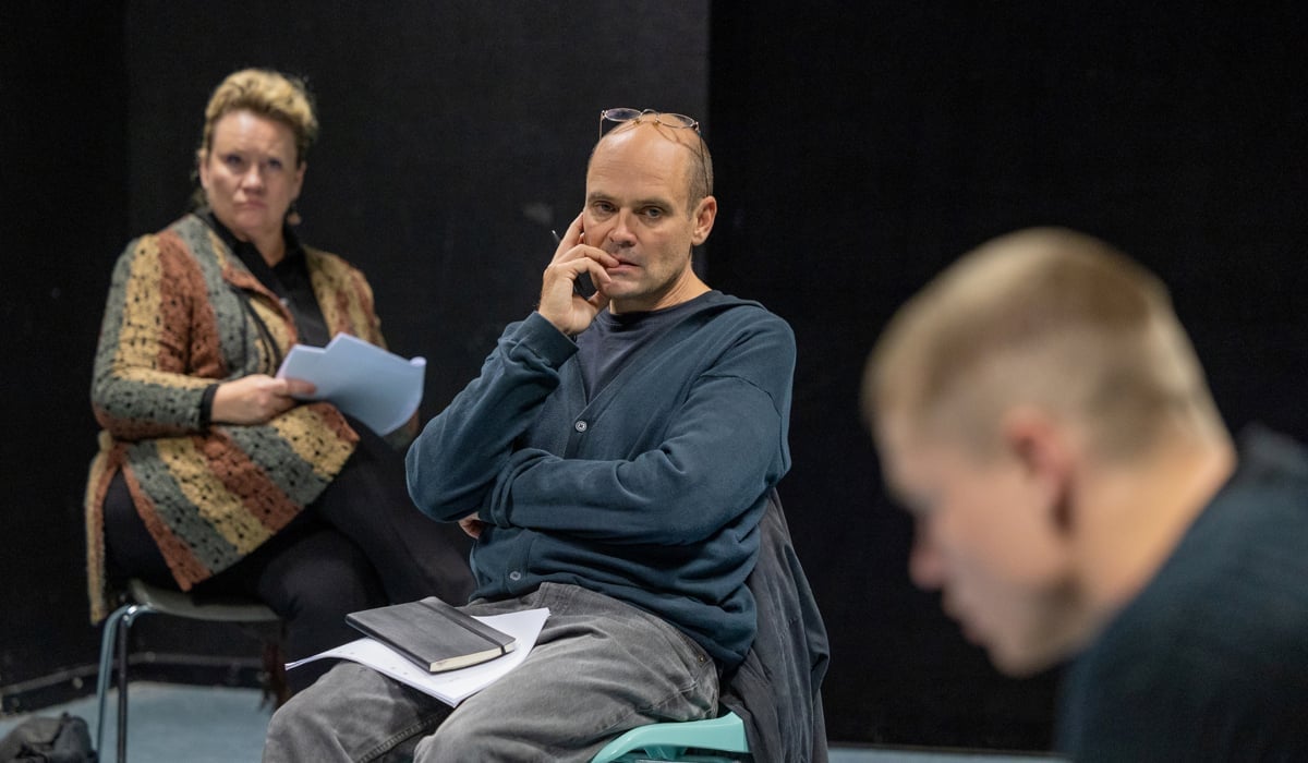 En man och en kvinna sitter på en teaterscen och betraktar en oskarp skådespelare i förgrunden.