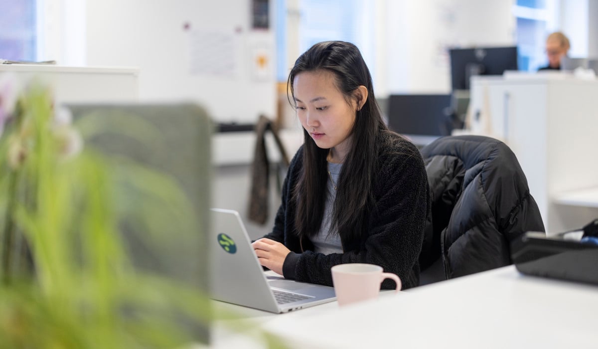Kvinna med asiatiskt utseende sitter och jobbar framför en dator.