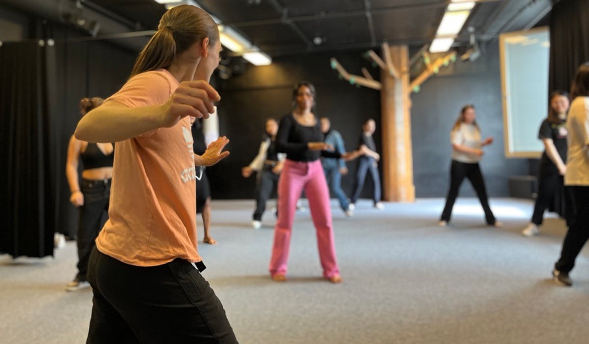 Dansinstruktör framför en grupp tjejer i träningskläder.