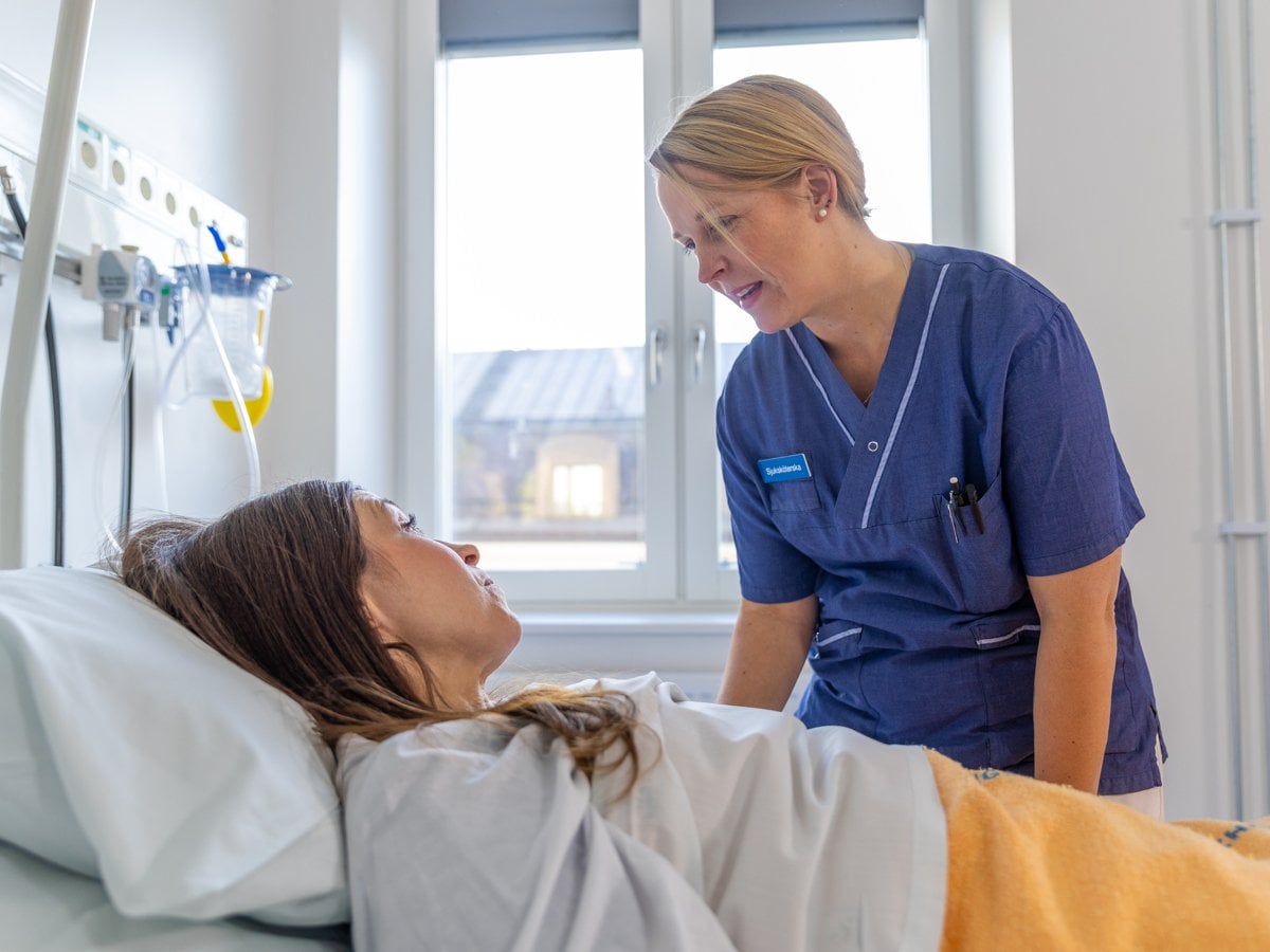 En sjuksköterska pratar med en patient i en sjukhussäng