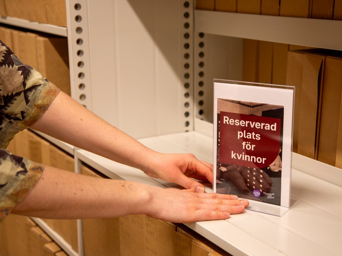 En kvinna placerar en skylt på en hylla i arkivet. På skylten står det Reserverad plats för kvinnor.