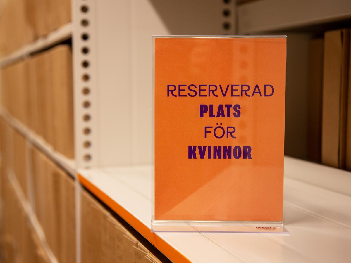 Orange skylt i en arkivhylla med texten reserverad plats för kvinnor.