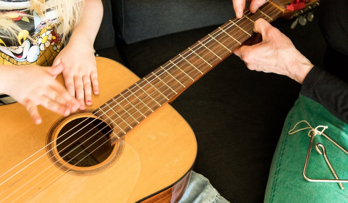 Barnhänder som trummar på en gitarr. En vuxen håller stadigt i gitarrhalsen.