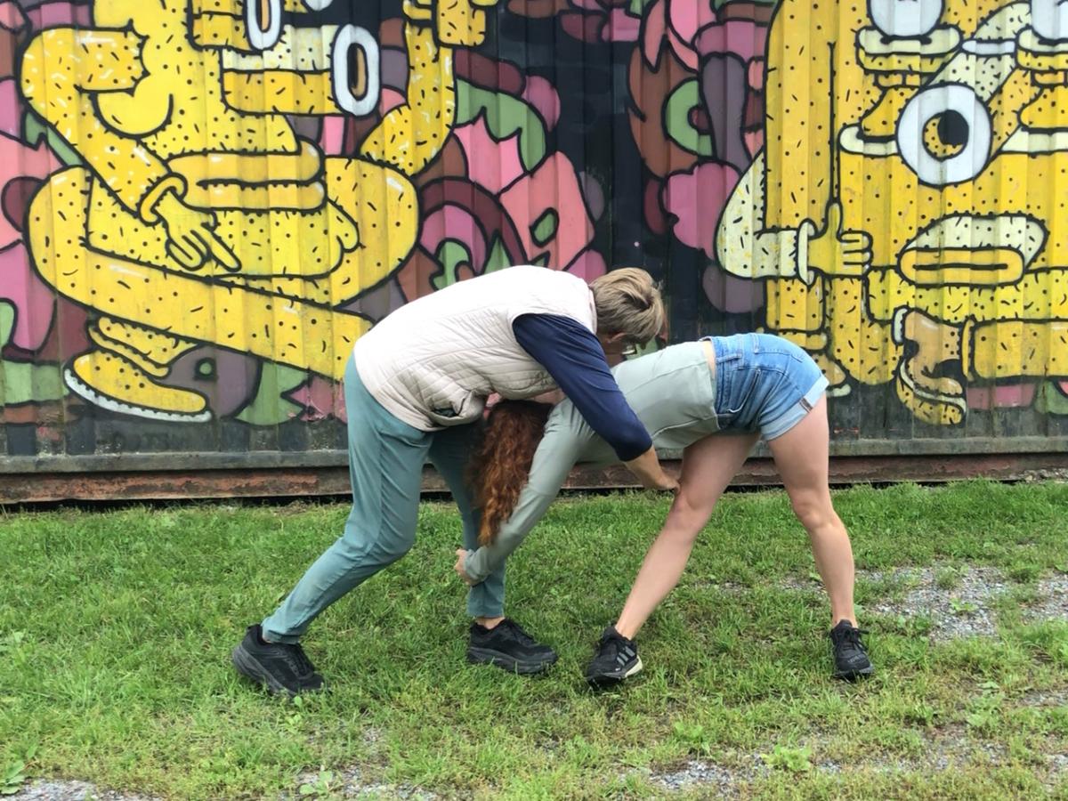 Två unga personer dansar framför plank med graffittimålning.