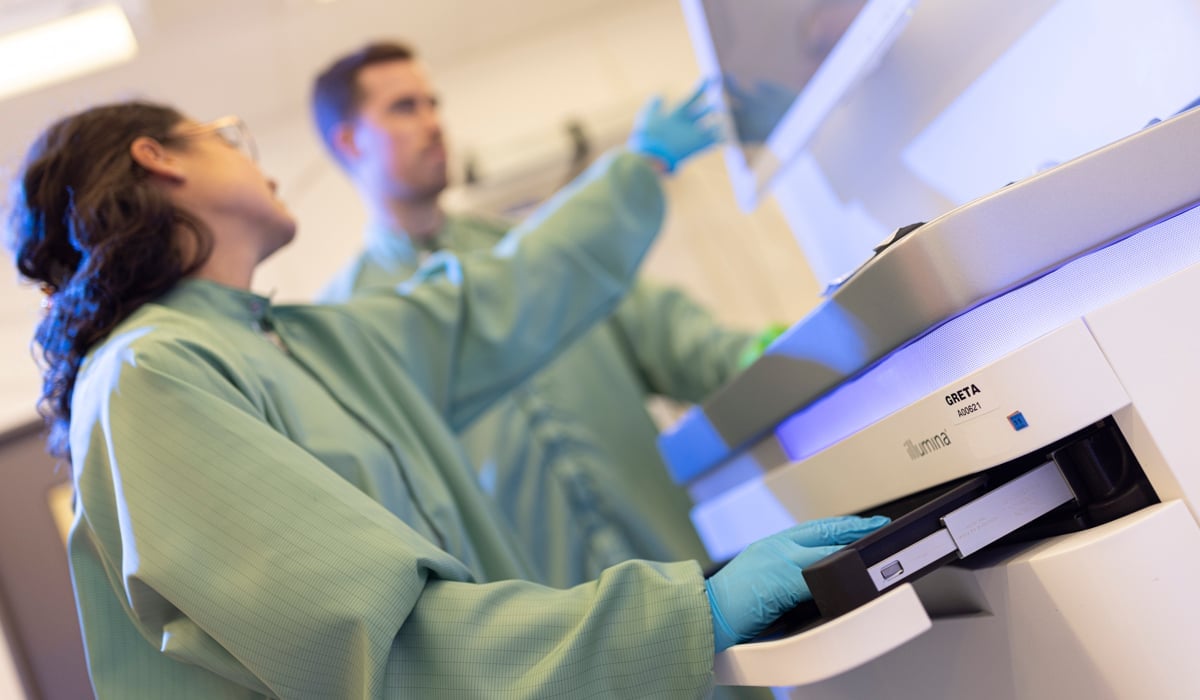 Två forskare i gröna rockar som står vid en maskin i ett laboratorium