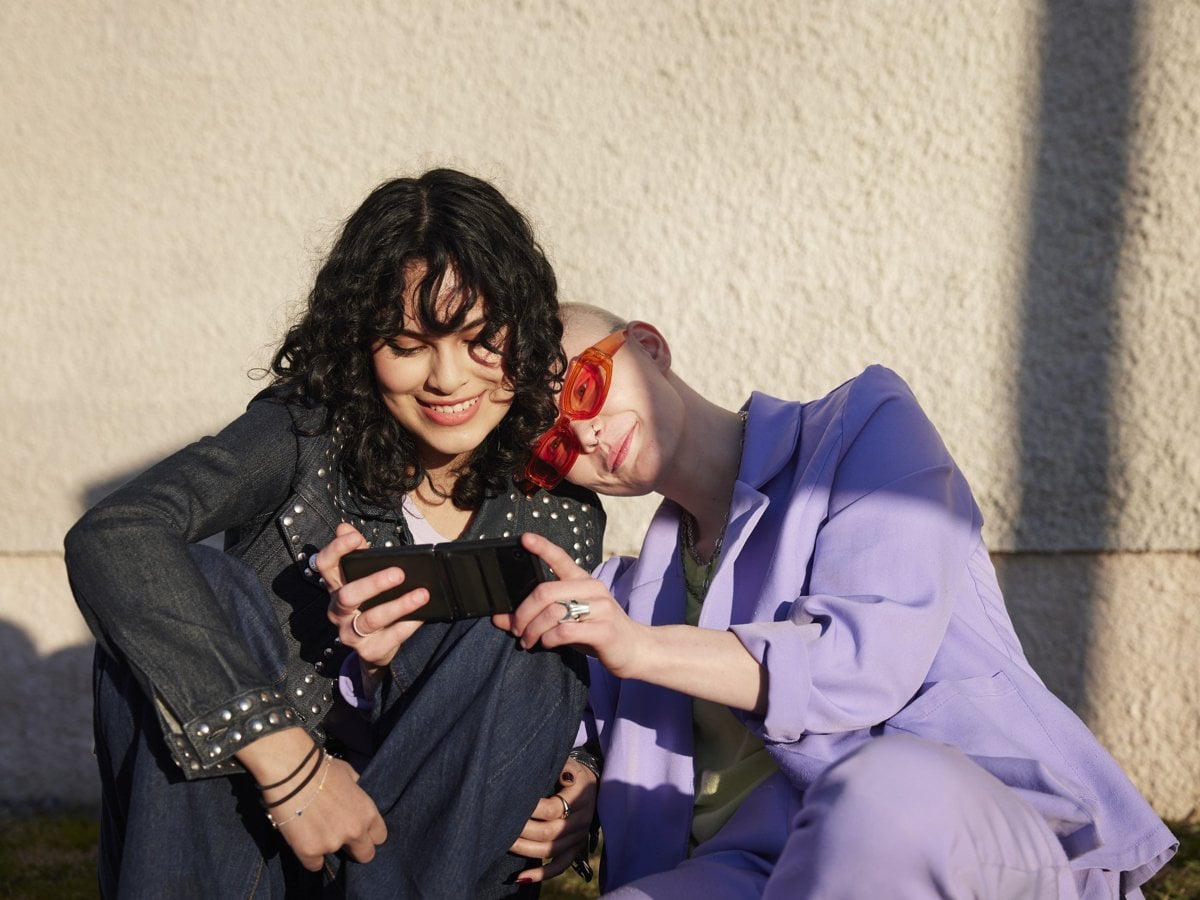 Foto på två tjejer som sitter och tittar på en mobil.