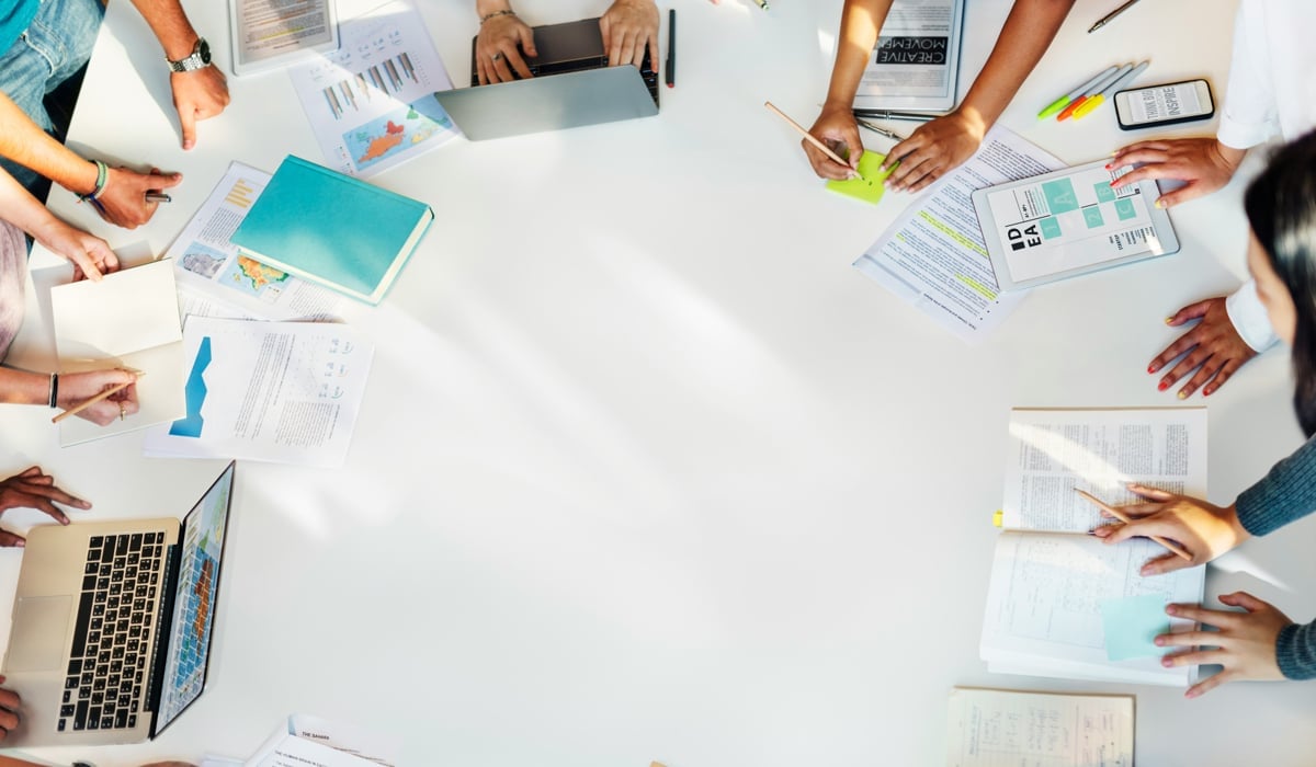 En grupp människor som sitter runt ett bord med bärbara datorer.