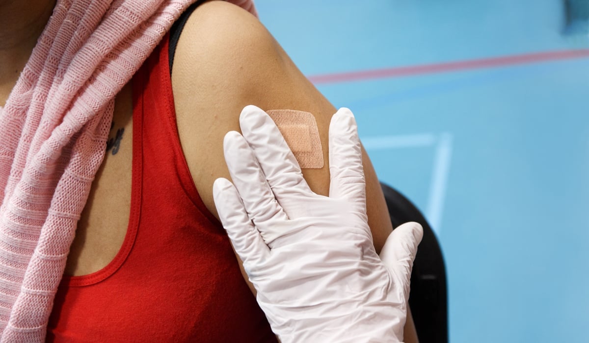 Ett plåster som sätts på en överarm av en behandskad hand