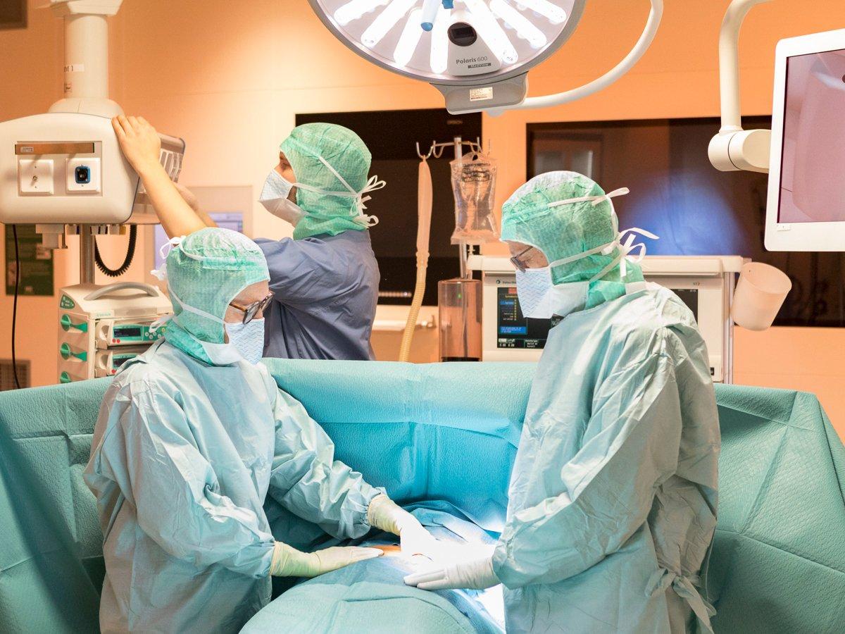 Tre personer i operationskläder i operationssal med patient.
