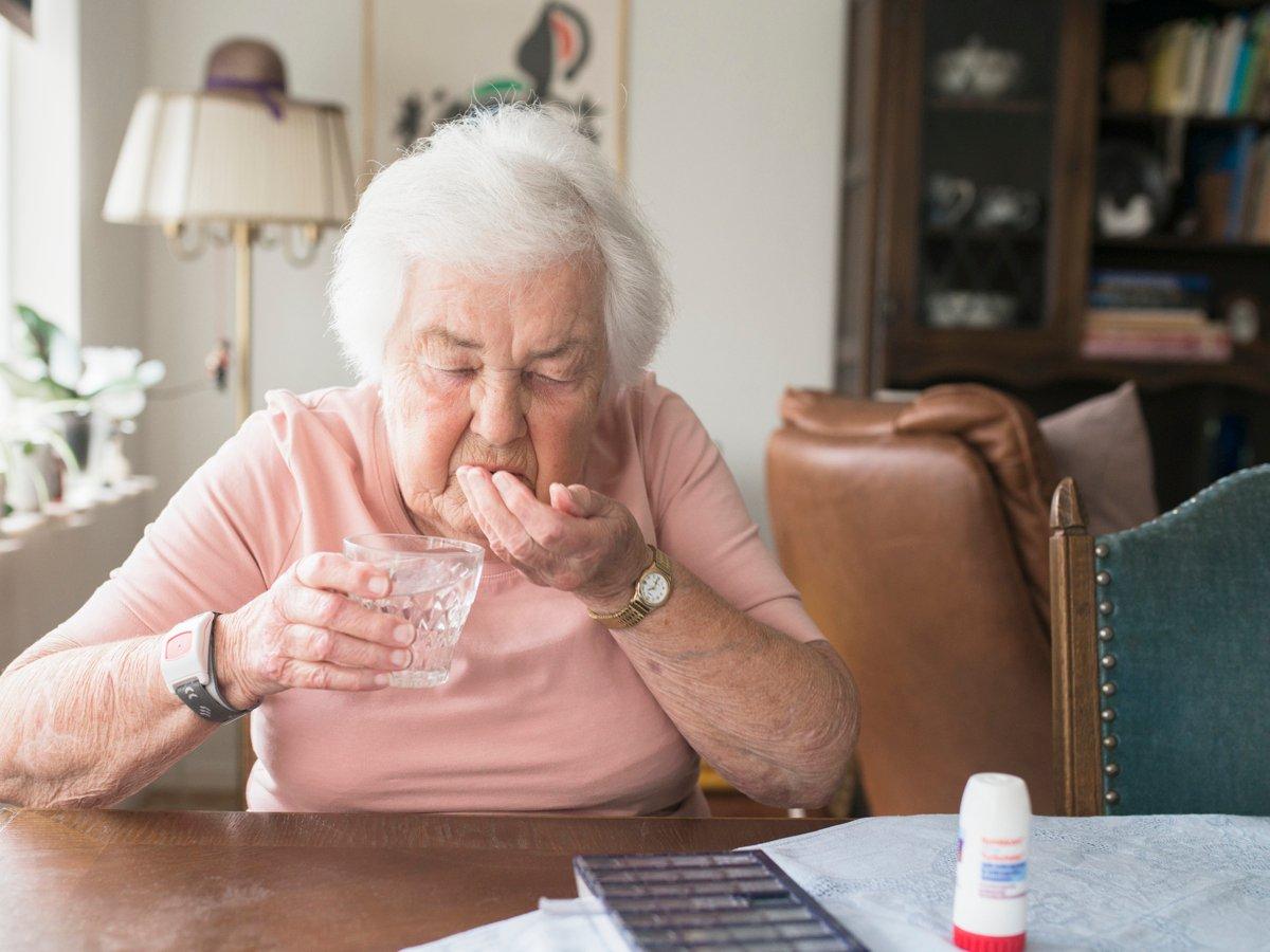 Äldre kvinna tar sin medicin. På bordet en dosett och en inhalator.