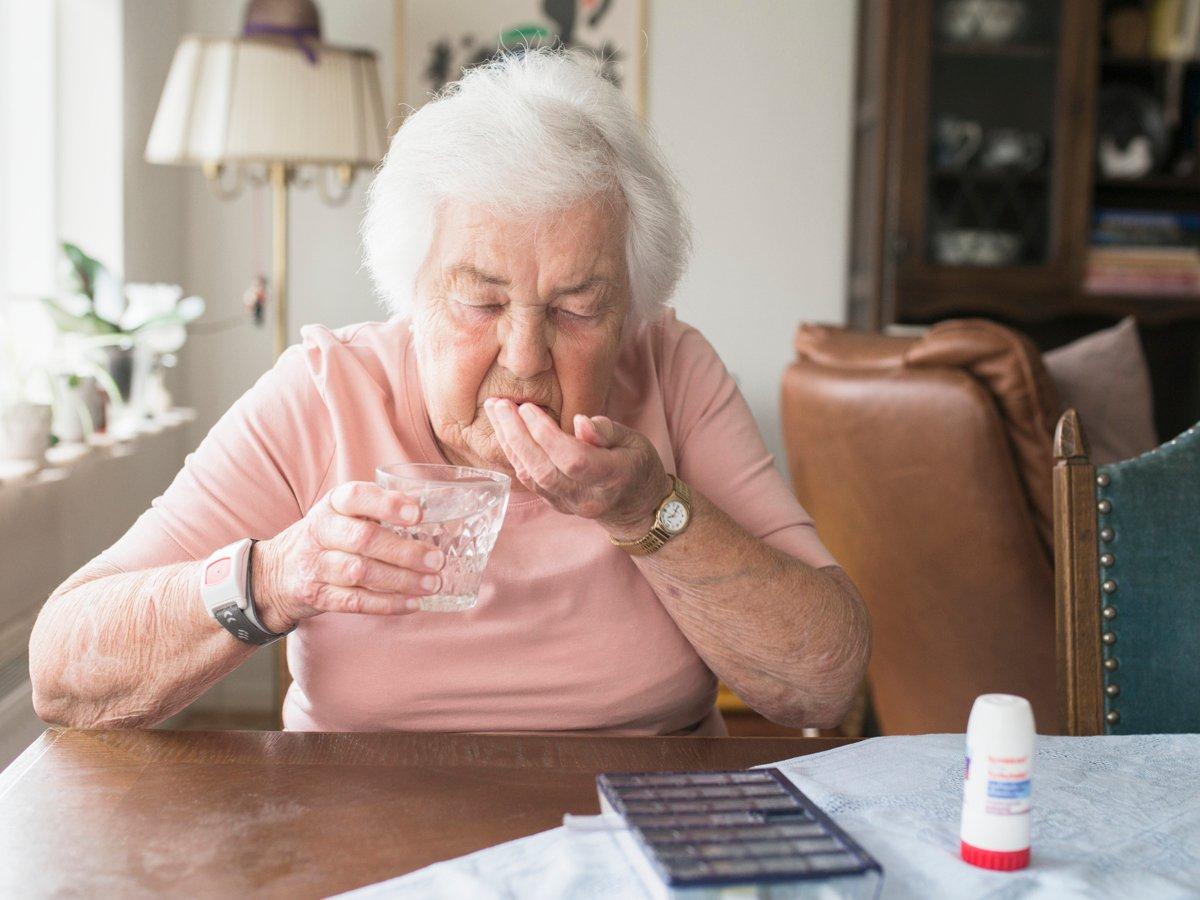 Äldre kvinna tar medicin. På bordet en dosett och en inhalator.