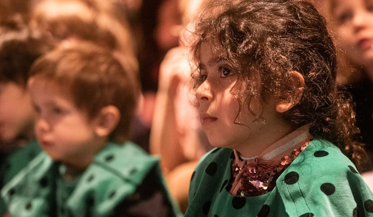 En grupp barn som sitter bredvid varandra i publik.
