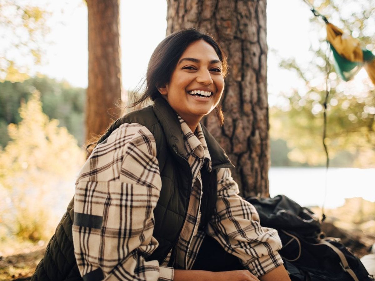 Foto på en kvinna som sitter i en skog. Hon ler in i kameran.