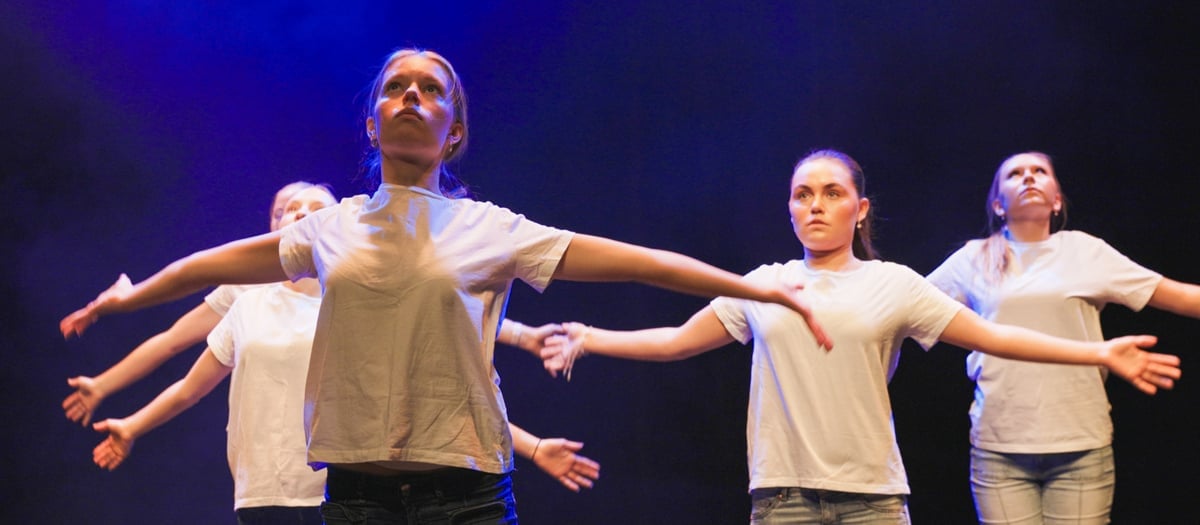 Fyra unga kvinnor i vita t-shirts och jeans dansar med utsträckta armar.