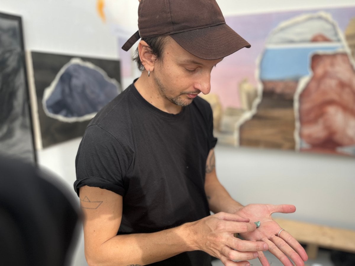 Vinícius dos Santos i ateöjén framför målningar på väggarna. Han har keps och plockar med något i händerna.