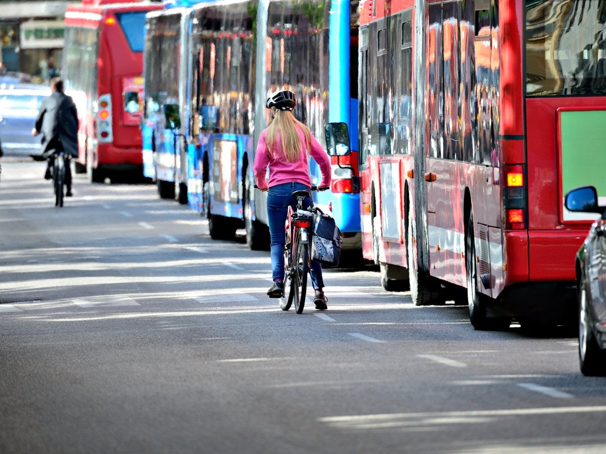 Foto på en kvinna som cyklar bredvid flera bussar.