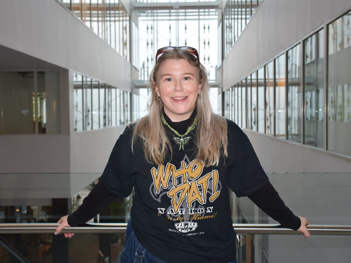Amanda ler mot kameran. Hon står i ett trapphus med händerna mot ett räcke.