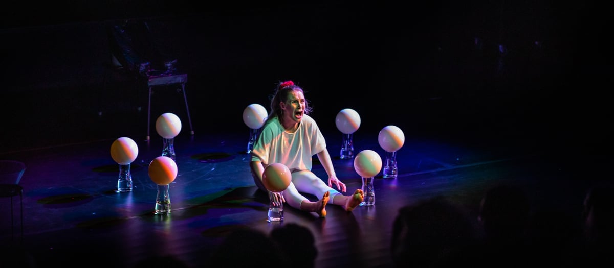 En person som sitter på en scen och ser rädd ut med ballonger runt sig.