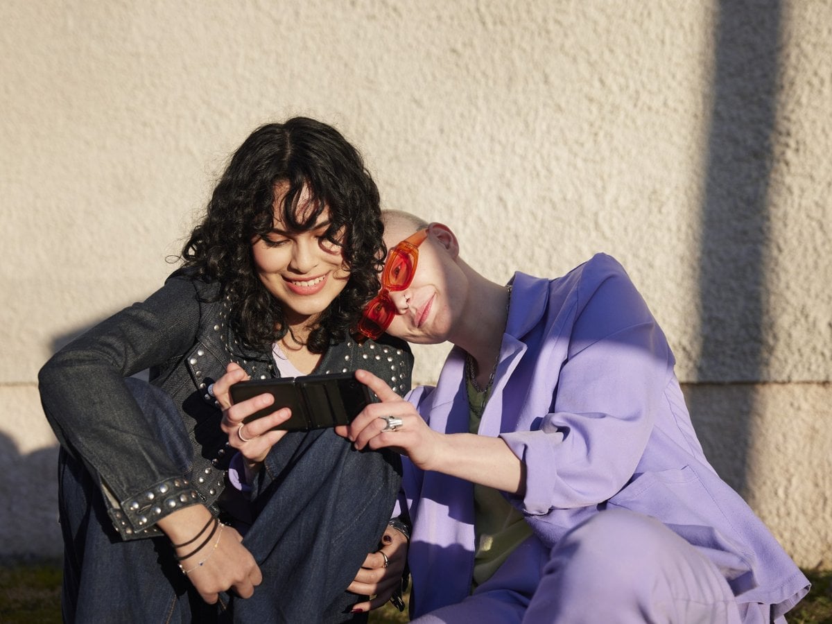 Foto på två tjejer som sitter och tittar på en mobil.