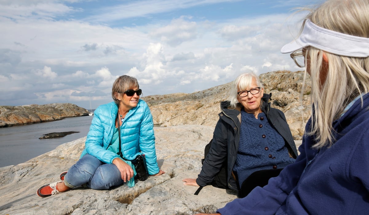 Tre kvinnor som sitter i en skärgårdsmiljö och pratar med varandra