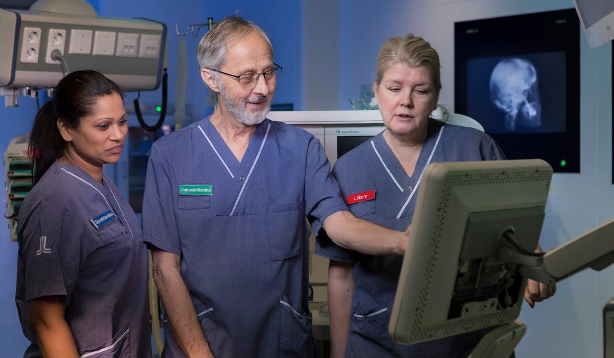 Tre personer klädda i sjukhuskläder som tittar på en skärm