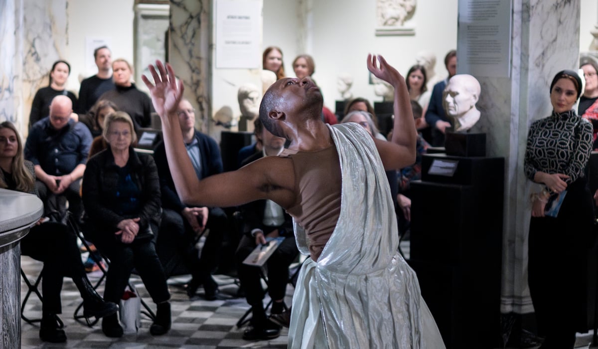 En person i vit klänning dansar framför en folkmassa.