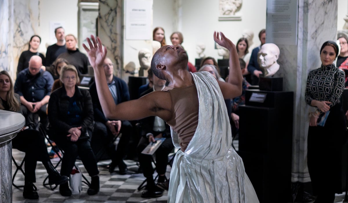 En person i vit klänning dansar framför en folkmassa.