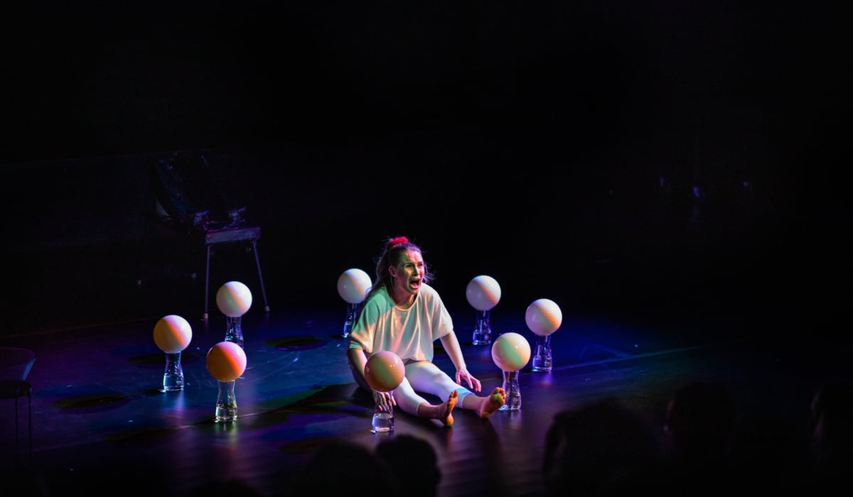 En person som sitter på en scen och ser rädd ut med ballonger runt sig.