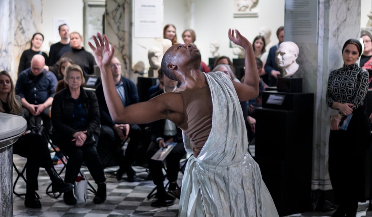 En person i vit klänning dansar framför en folkmassa.