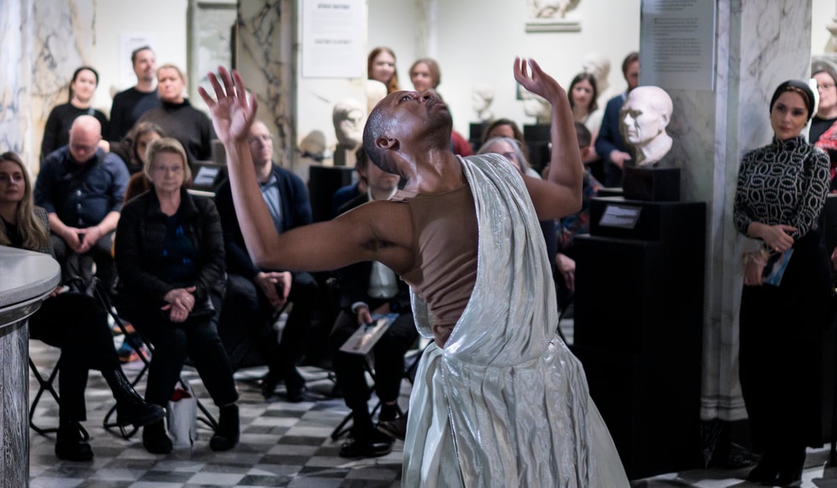 En person i vit klänning dansar framför en folkmassa.