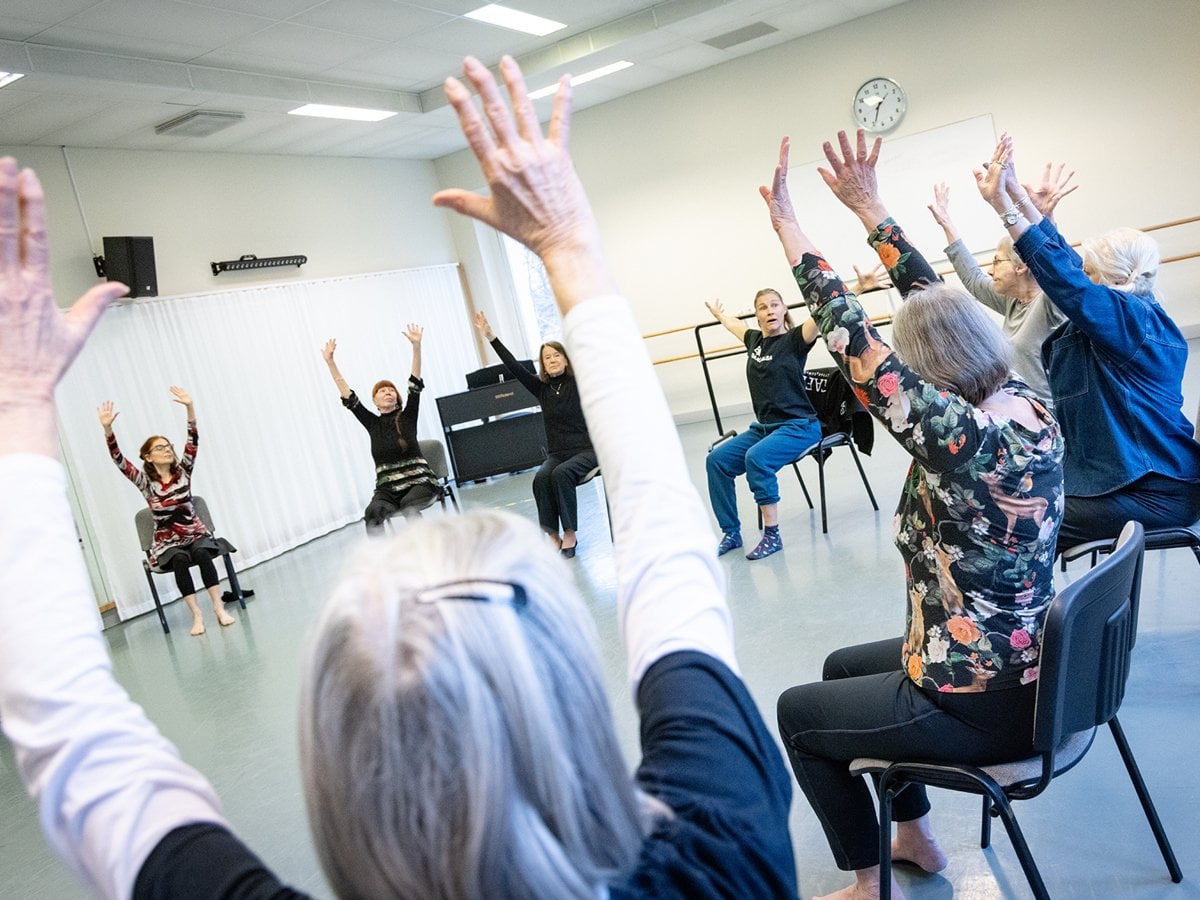 Grupp äldre sitter i ring med armar upp i luften.