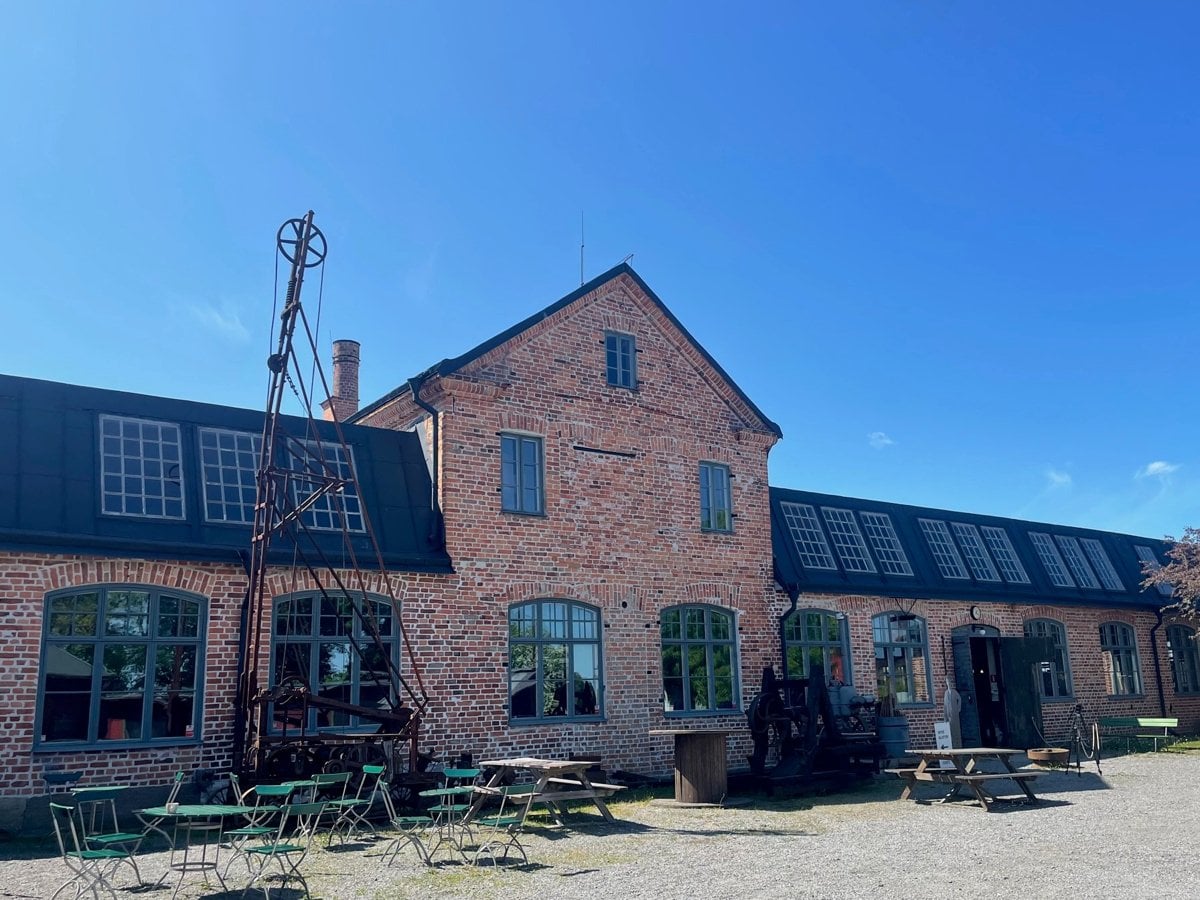 Exteriör Pythagoras industrimuseum. Röd tegelbyggnad med utemöbler framför på gårdsplan.