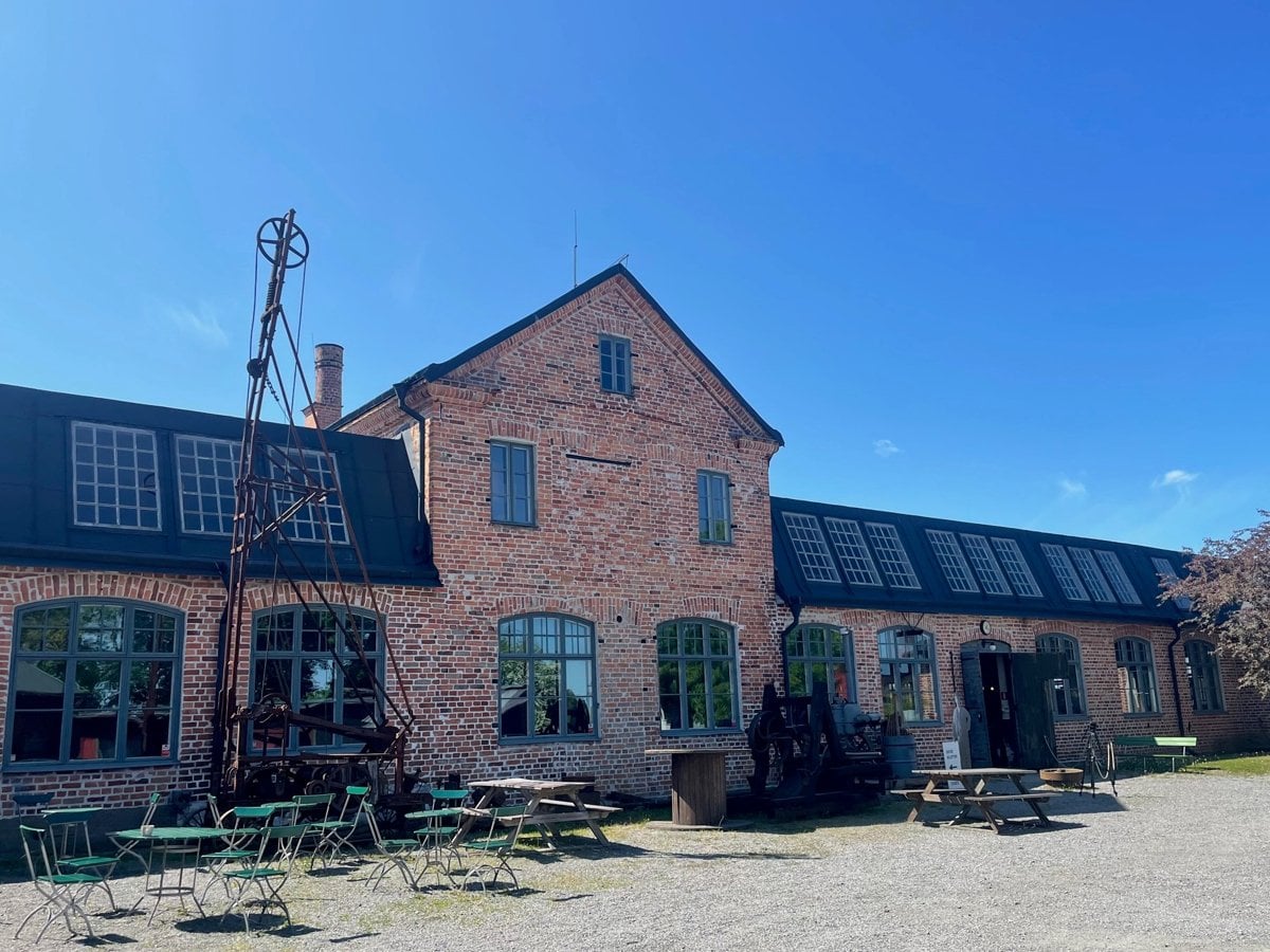 Exteriör Pythagoras industrimuseum. Röd tegelbyggnad med utemöbler framför på gårdsplan.