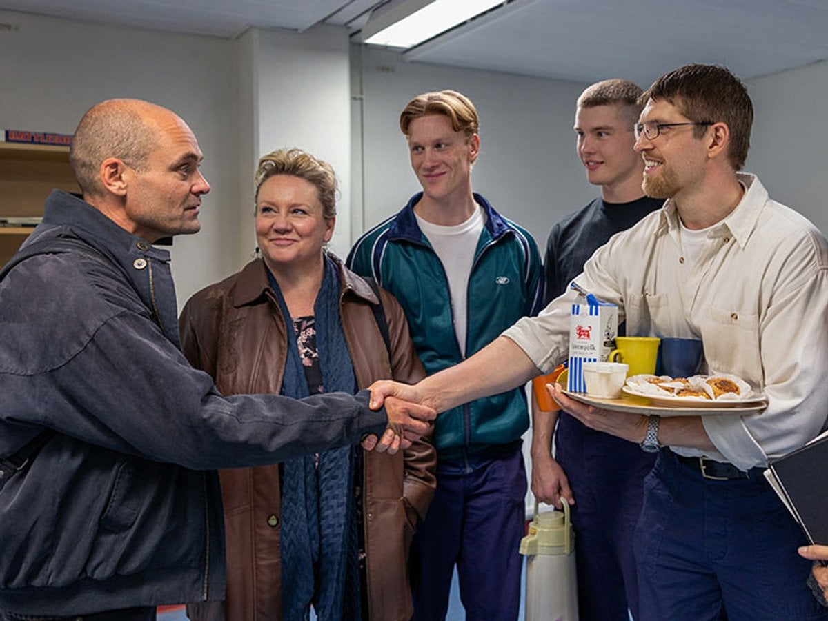 David Dencik som Lars Norén skakar hand med internerna i ett kontorsrum.