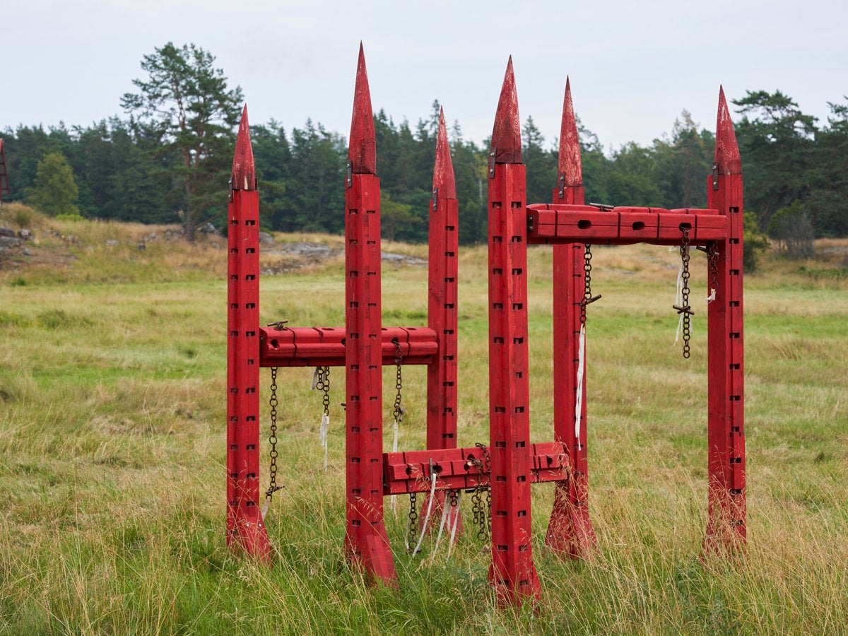 En rödfärgad skulptur i trä på ett fält.