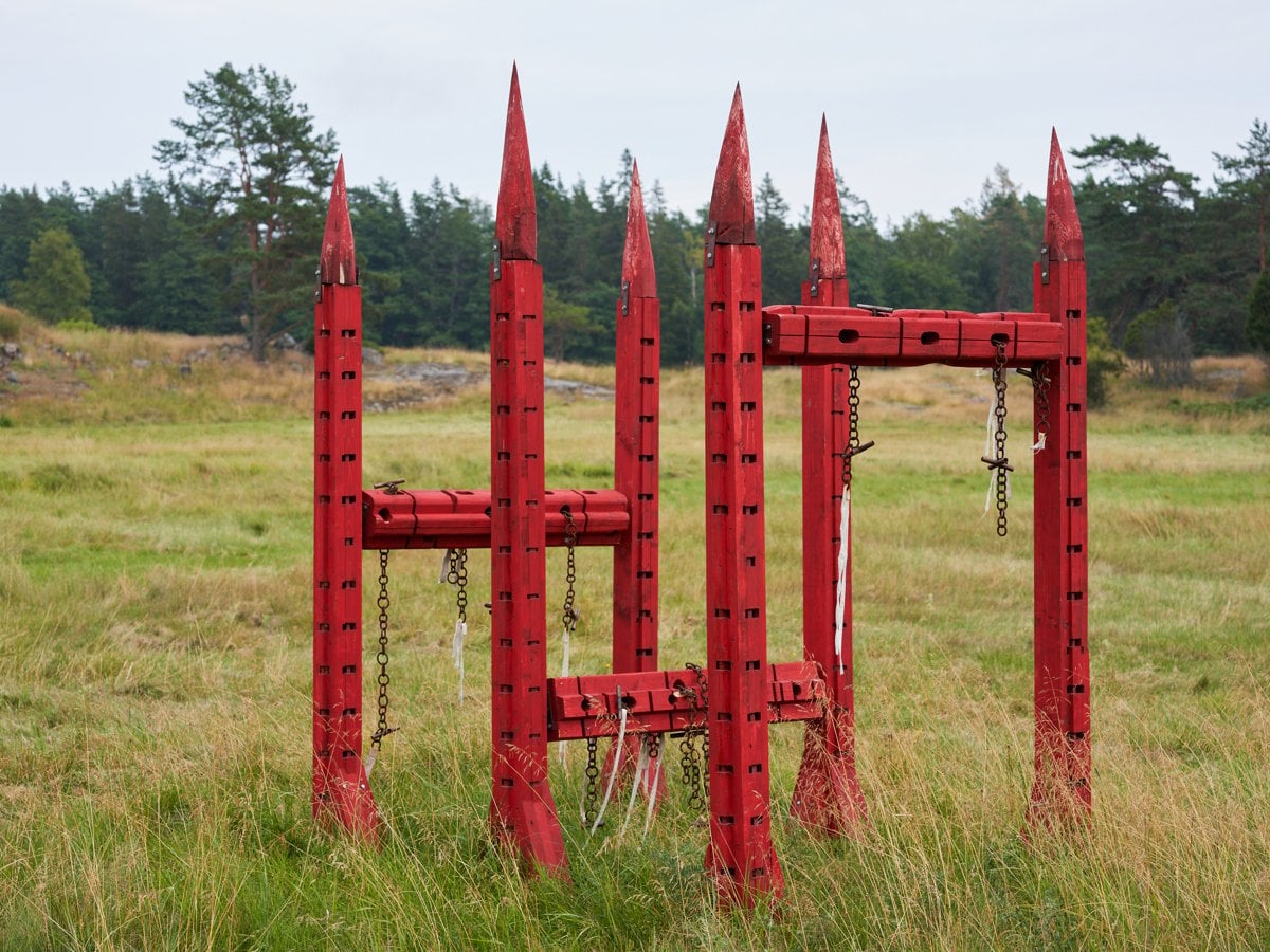 En rödfärgad skulptur i trä på ett fält.