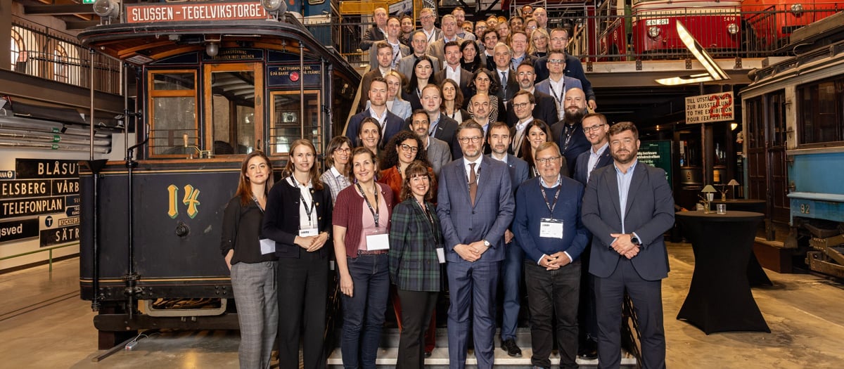 En grupp människor som står i en lång trappa, bland tåg och bussar på Spårvägsmuseet.