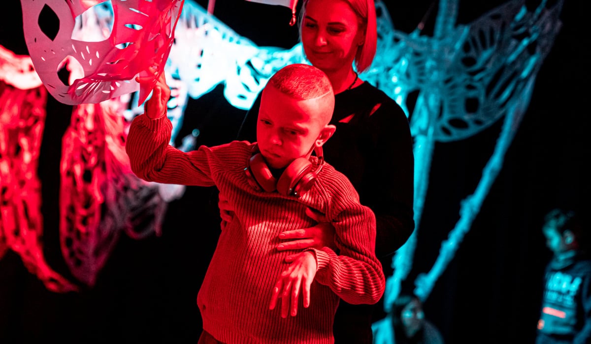 Ett barn som har svårt att röra sig rör sig med stöd av en vuxen på en scen med färgglada dekorationer