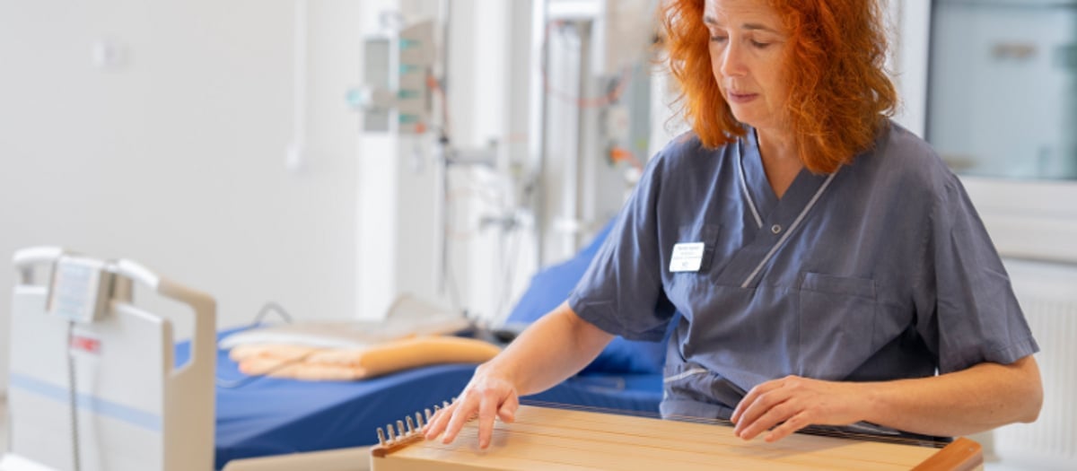 Pernilla sitter med instrument i knät. Bakom skymtar en sjukhussäng.