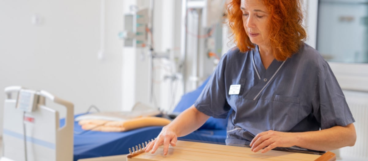 Pernilla sitter med instrument i knät. Bakom skymtar en sjukhussäng.