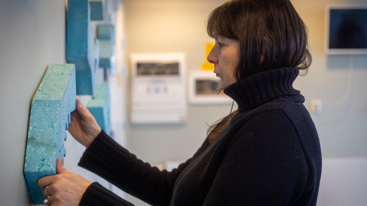 En kvinna i svart tröja hänger upp ett konstverk på en vägg.