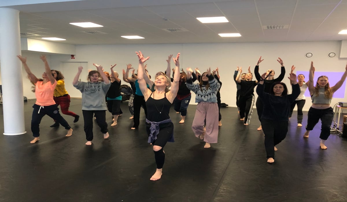 Två händer som håller varandra. I bakgrunden anas tre personer som sitter ner som också håller varandra i händerna.