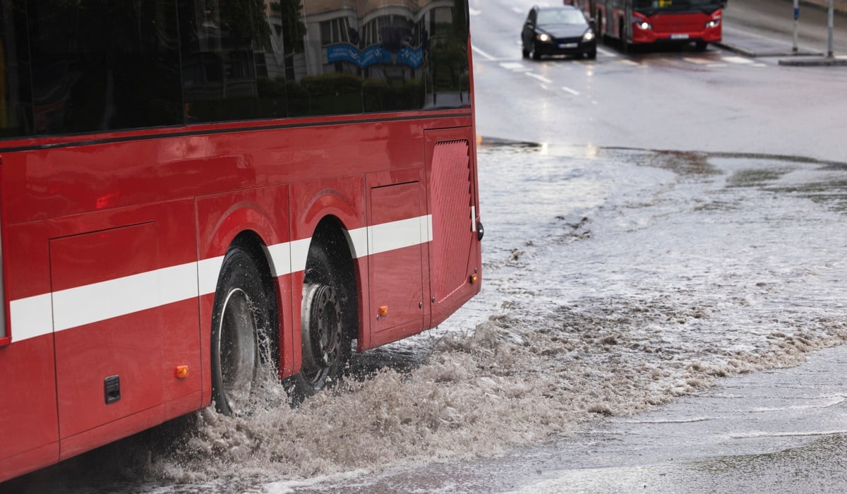 En röd buss som kör genom en översvämmad gata.