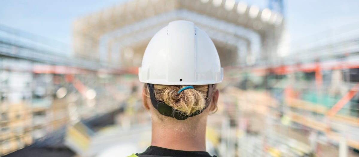 På bilden syns en byggarbetare i hjälm bakifrån på en byggarbetsplats.