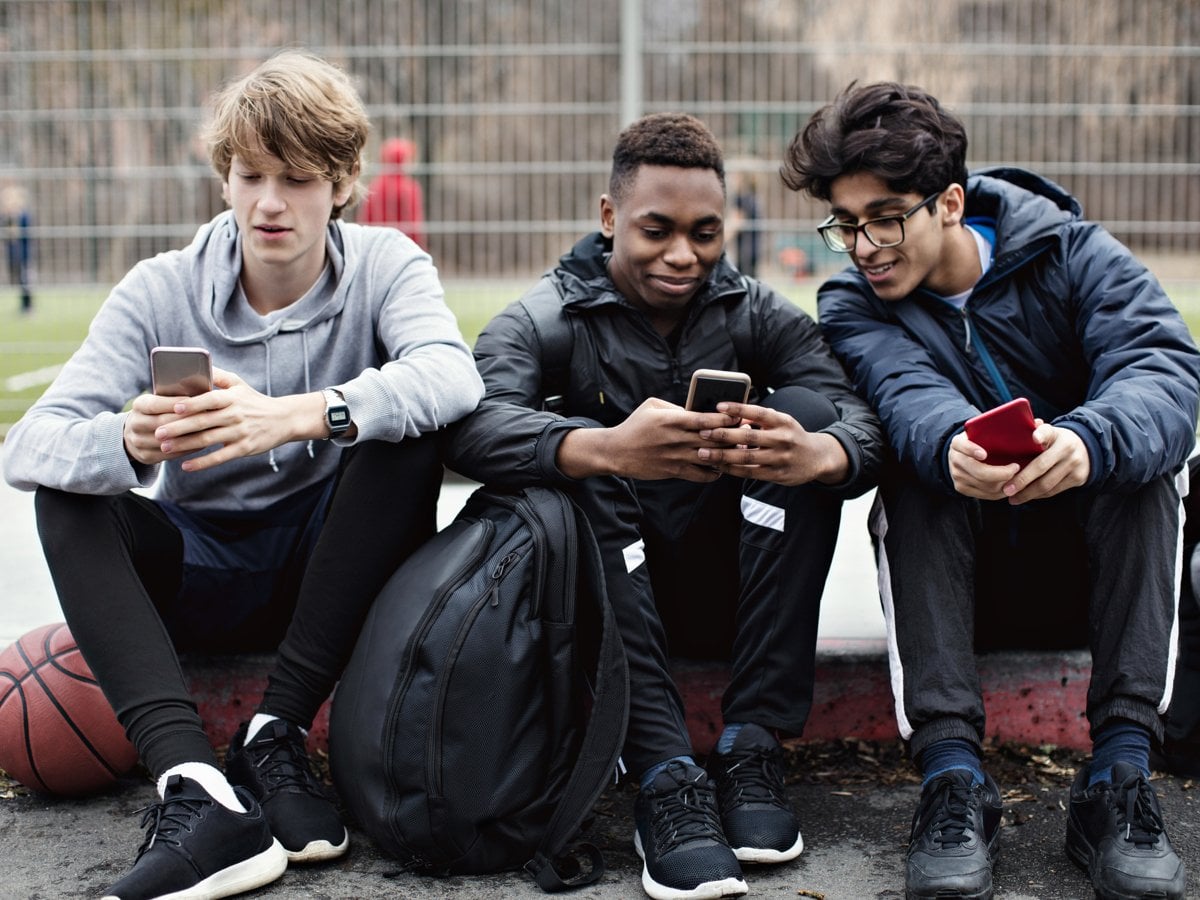 Tre unga personer sitter bredvid varandra och tittar i sina mobiler.