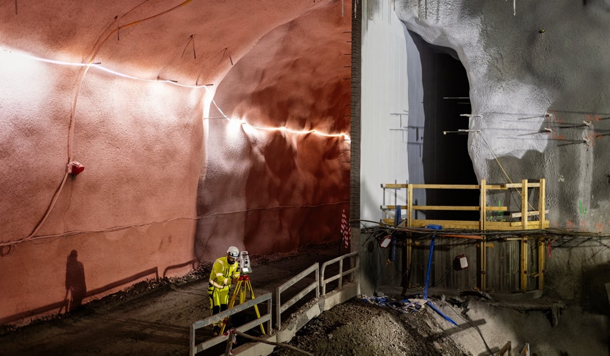 En man i gul jacka står i tunnel med mätverktyg.