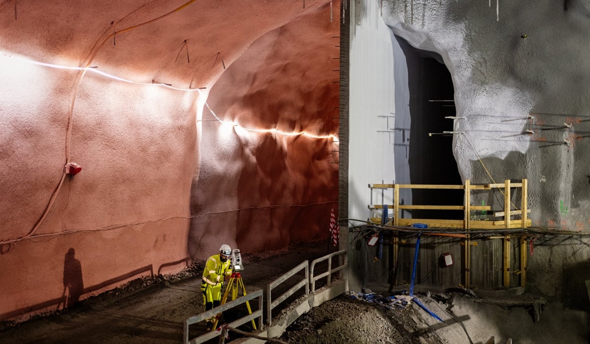 En man i gul jacka står i en tunnel med ett mätverktyg.