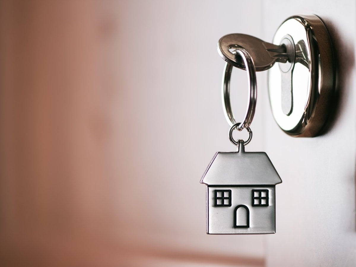 Foto på en nyckel som sitter i ett lås. Nyckeln har en nyckelring med ett hus.
